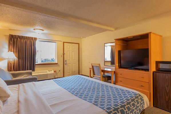 Quarto de hotel com cama, escrivaninha, televisão e cômoda.