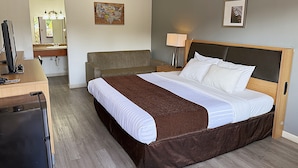 Une chambre d’hôtel avec un lit, un bureau, une chaise, une lampe et un miroir.