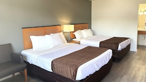 Une chambre d’hôtel avec deux lits, une table de chevet avec une lampe, une chaise et une salle de bain avec un miroir et un lavabo.