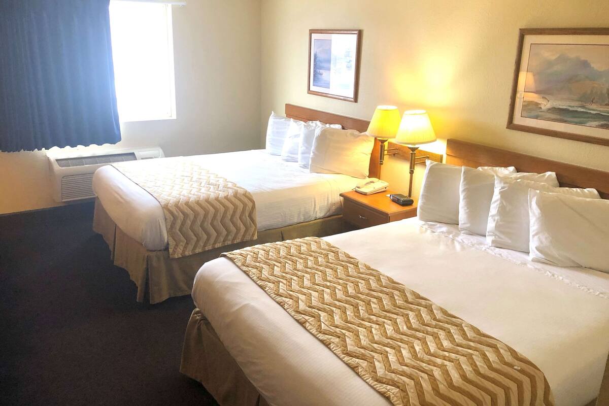 Habitación de hotel con dos camas, una mesita de noche con lámpara, un cuadro en la pared y una ventana con cortinas.
