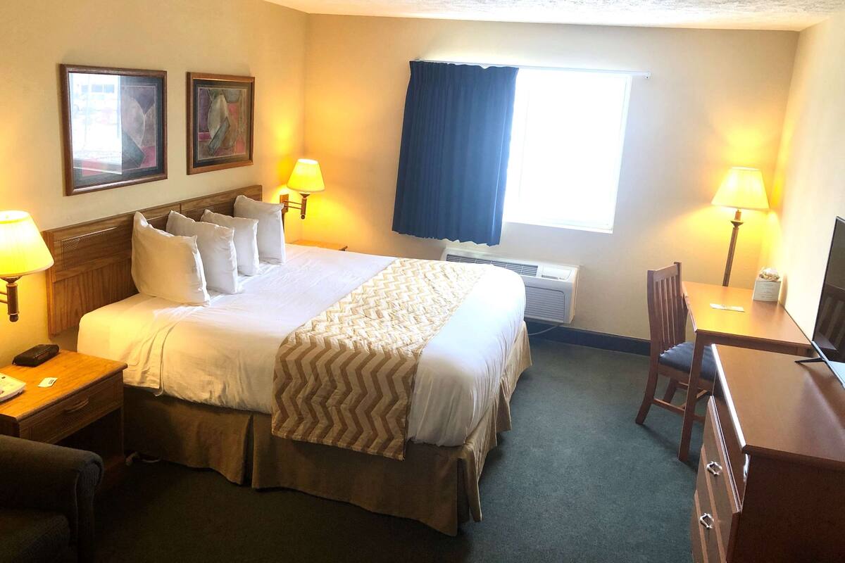 Una habitación de hotel con una cama grande, dos lámparas de noche, un escritorio con una silla y una ventana con cortinas.