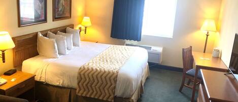 A hotel room with a large bed, two bedside lamps, a desk with a chair, and a window with curtains.