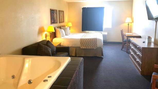 A hotel room with a bed, a desk, a chair, a TV, and a bathtub. - Travelodge by Wyndham Grand Island (Grand Island)