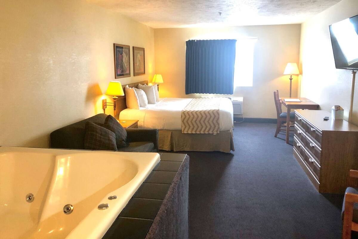 Una habitación de hotel con cama, escritorio, silla, televisor y bañera.