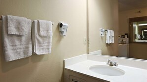 A bathroom with a white sink, two towels hanging on the wall, and a hair dryer mounted on the wall. - Travelodge by Wyndham Grand Island (Grand Island)