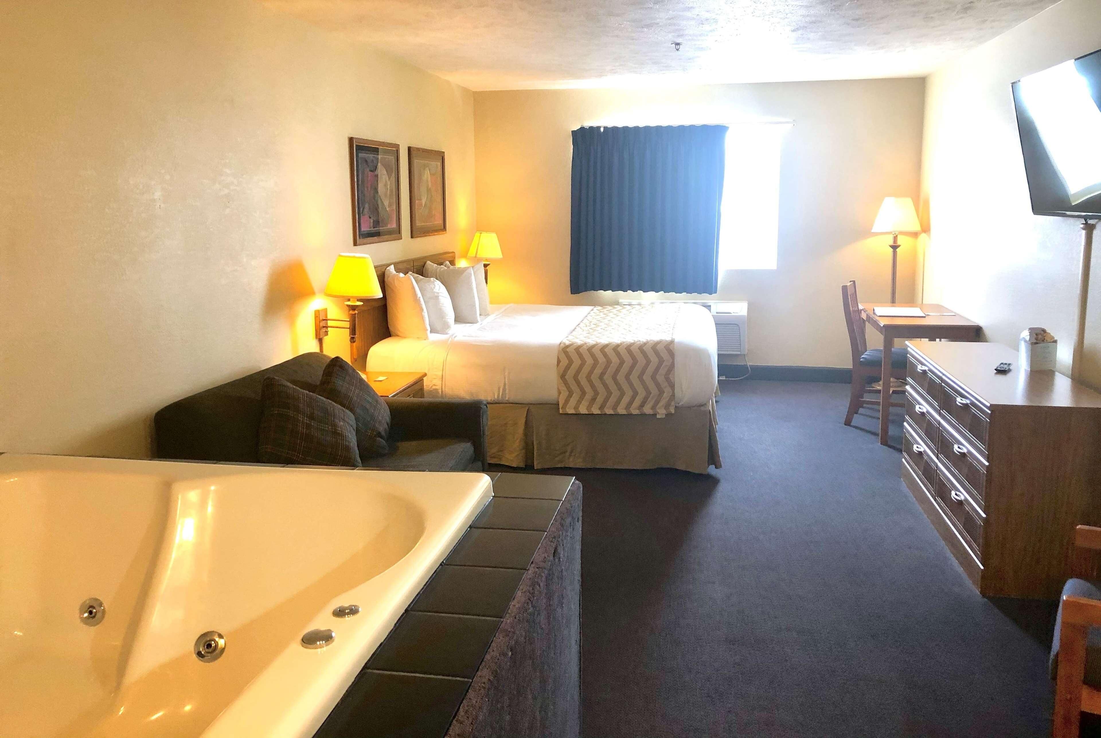 A hotel room with a bed, a desk, a chair, a TV, and a bathtub.