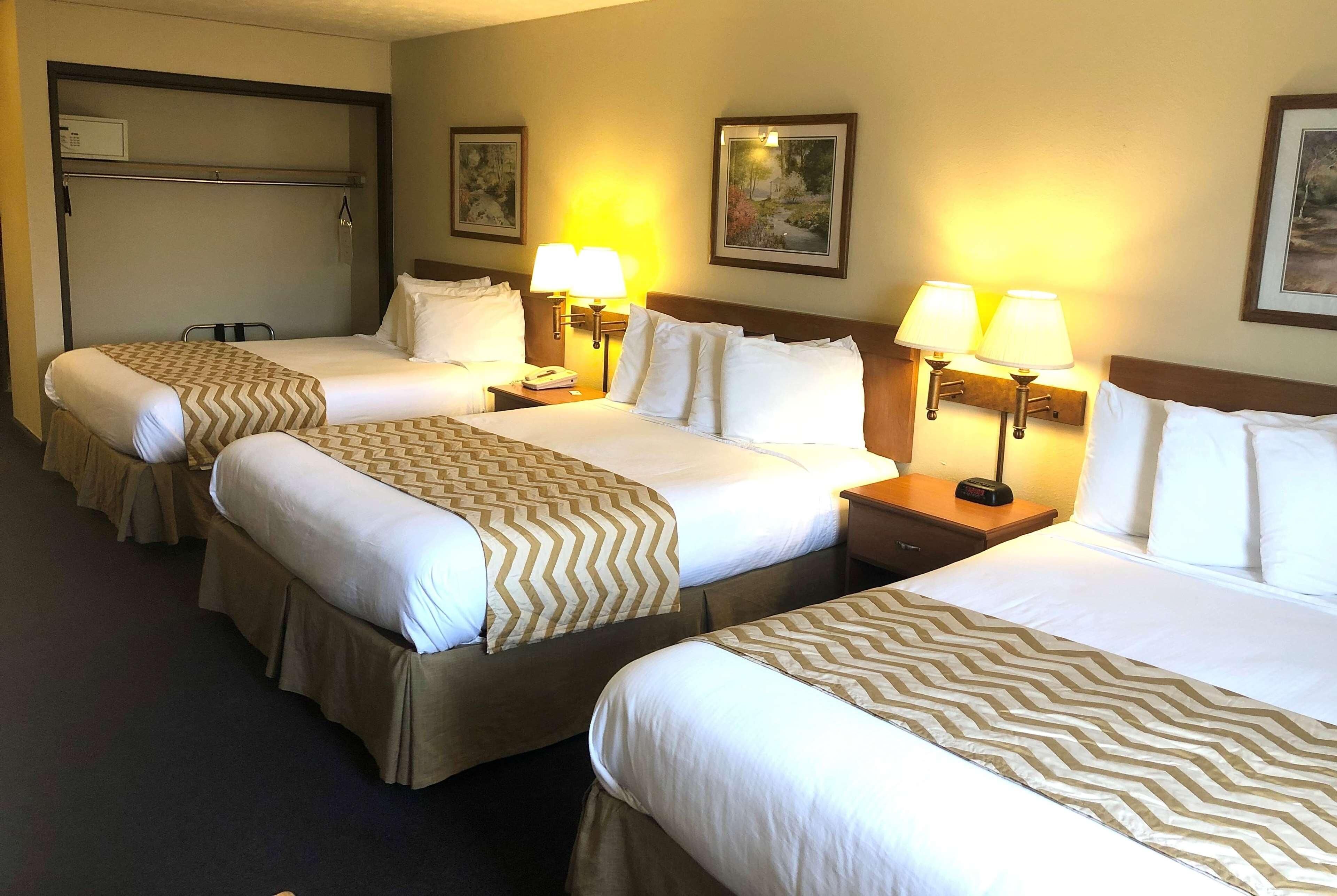 A hotel room with three beds, each with a patterned bedspread, bedside lamps, and framed artwork on the walls.