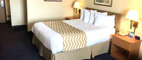 A neatly made bed with a patterned bedspread, two bedside lamps, a nightstand with a phone, and two framed pictures on the wall.