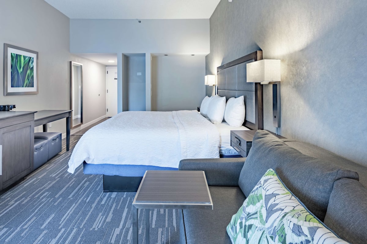 Una habitación de hotel moderna con una cama grande, un sofá, una mesita, un escritorio y una lámpara.