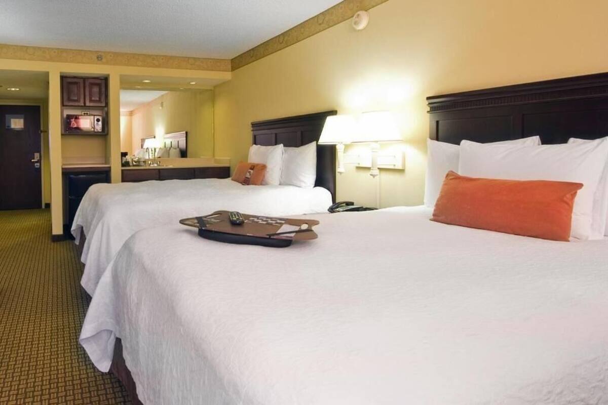 A hotel room with two beds, a desk, and a mirror.