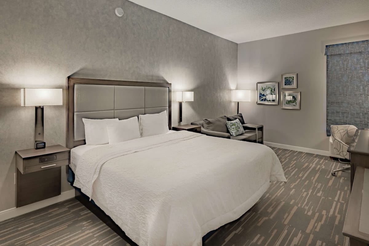 Una habitación de hotel con una cama grande, dos mesitas de noche con lámparas, una silla y un escritorio.