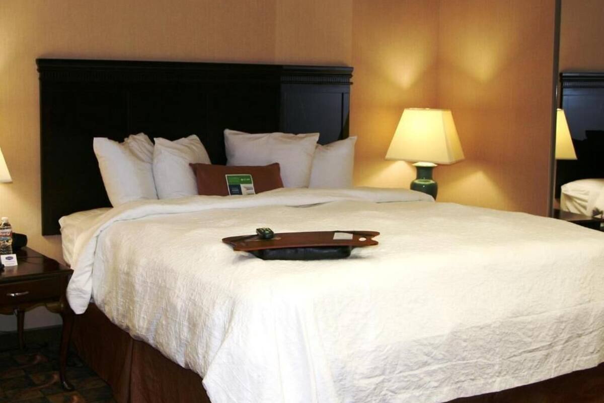 Una habitación de hotel con una cama grande, una mesita de noche con lámpara y una bandeja sobre la cama.