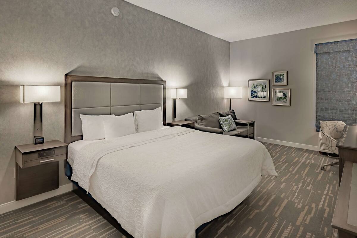 Una habitación de hotel con una cama grande, dos mesitas de noche con lámparas, una silla y un escritorio.