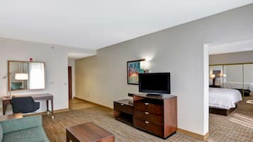 Quarto de hotel com escrivaninha, cadeira, televisão e cama.