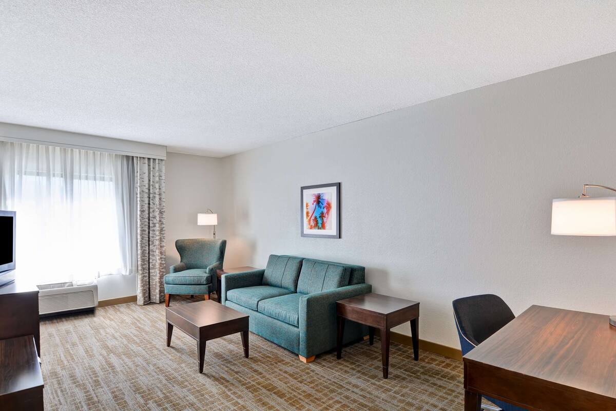 Quarto de hotel com sofá, duas poltronas, mesa de centro, televisão e quadro na parede.