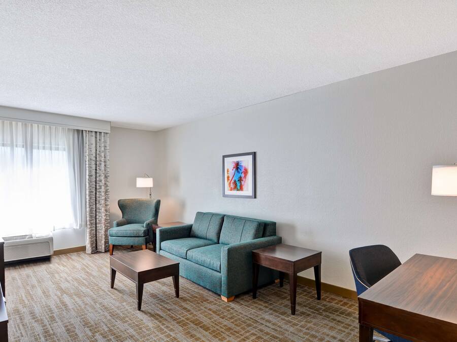 A hotel room with a sofa, two armchairs, a coffee table, a TV, and a painting on the wall.