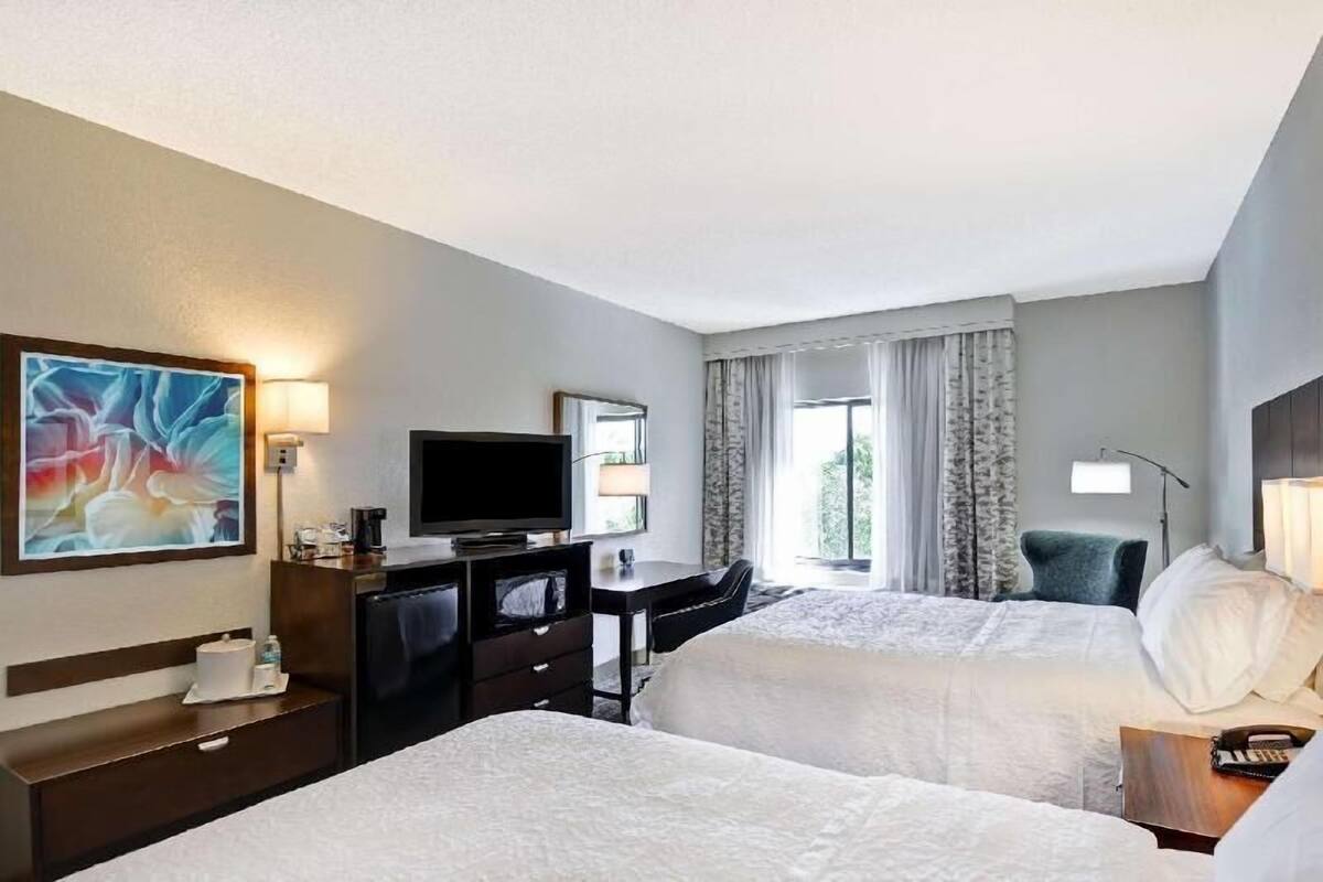 Quarto de hotel com duas camas, uma escrivaninha, televisão e um quadro na parede.