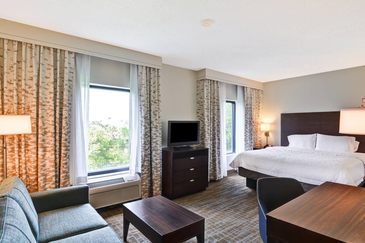 Quarto de hotel com uma cama, televisão em uma cômoda, escrivaninha e uma cadeira.