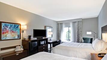 A hotel room with two beds, a desk with a television, a coffee machine, and a painting on the wall.