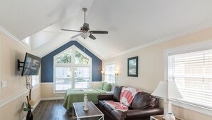 A living room with a brown leather couch, a white coffee table, a ceiling fan, and a TV mounted on the wall.