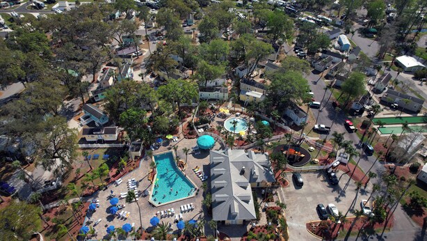 An aerial view of a residential area with a swimming pool, multiple houses, and parked cars.