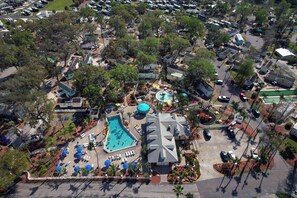 Vue aérienne d’un quartier résidentiel avec une piscine, plusieurs maisons et des voitures garées.
