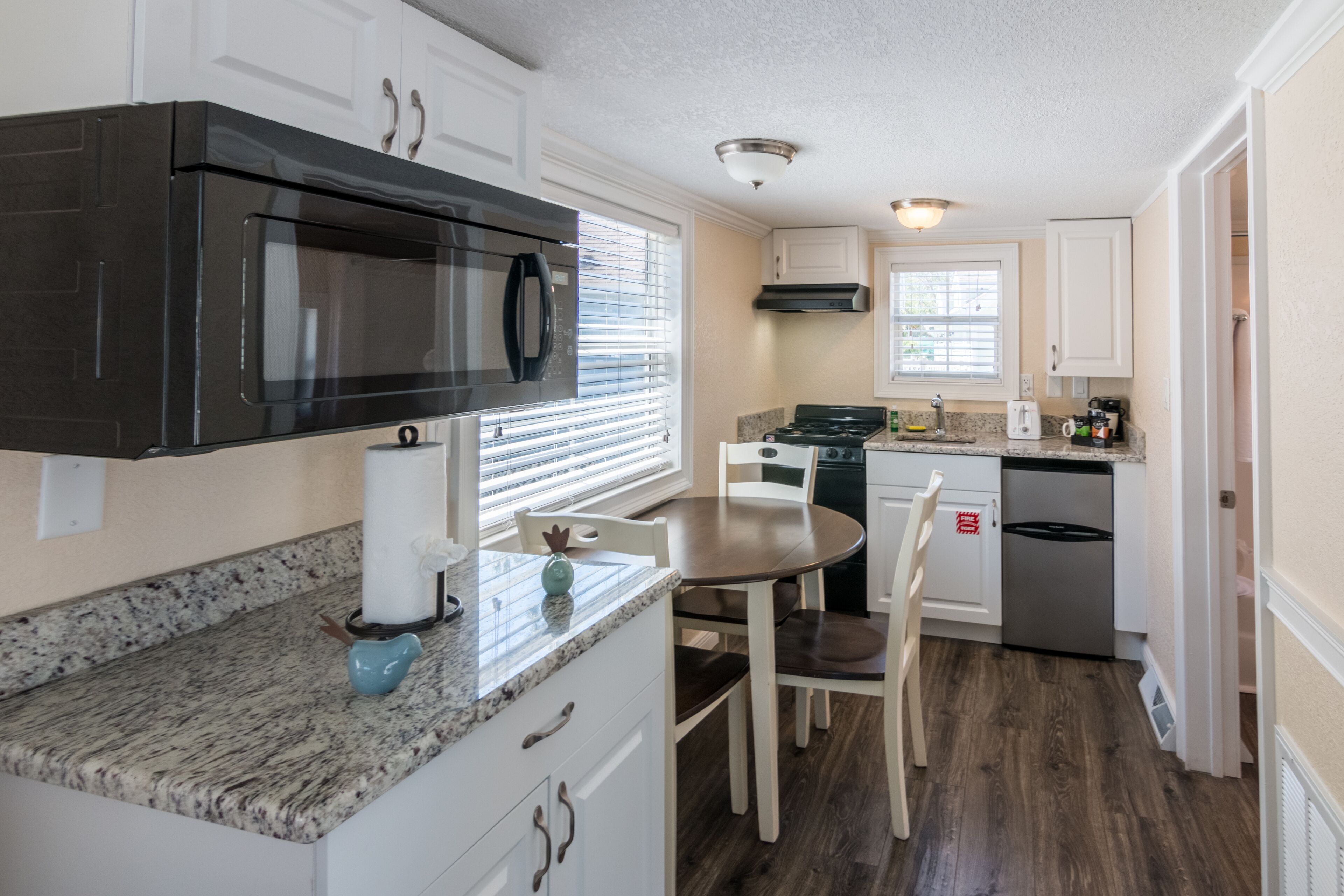 A kitchen with white cabinets, a black microwave, a stove, and a sink.