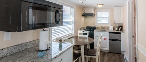 A kitchen with white cabinets, a black microwave, a stove, and a sink.