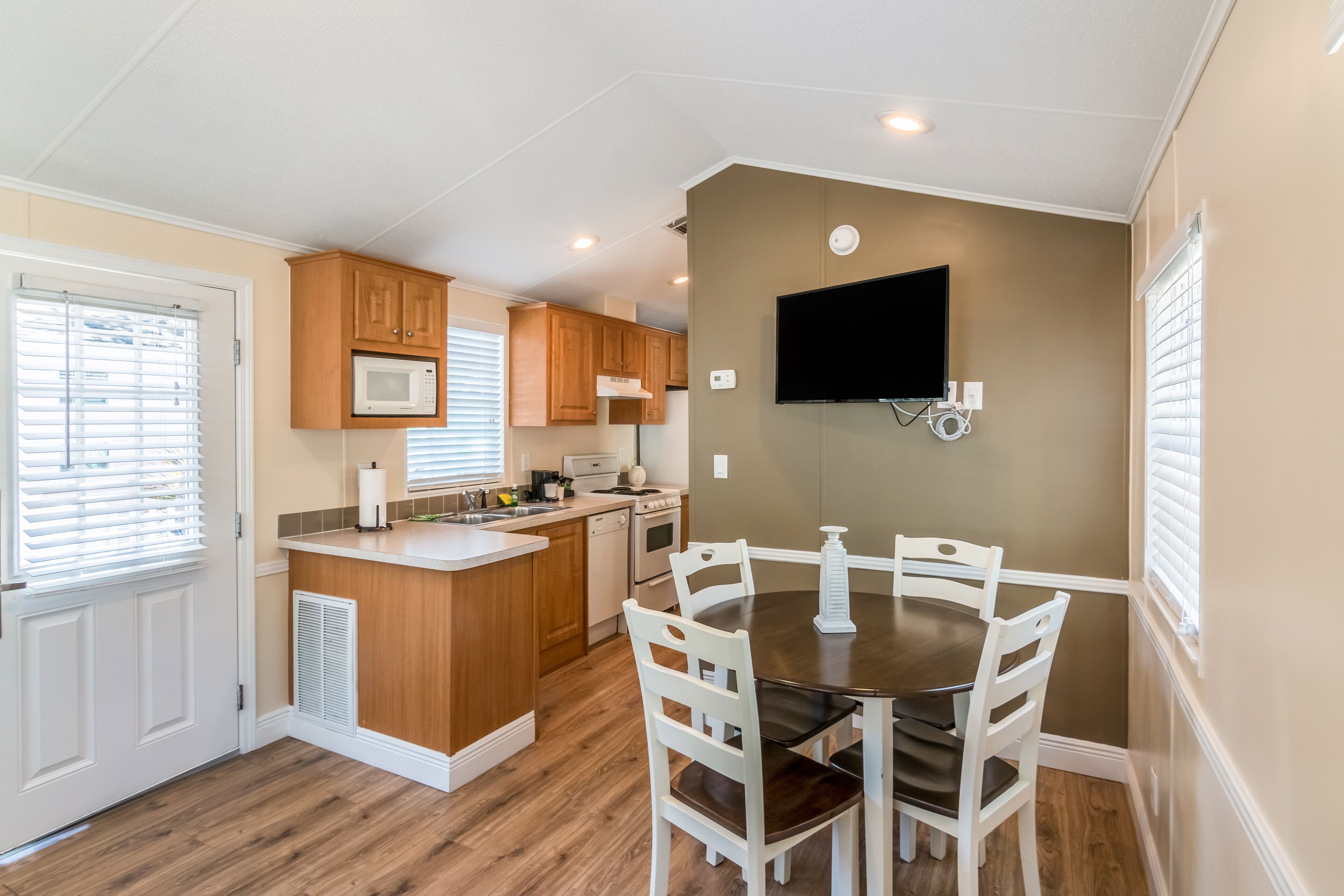 A compact kitchen with wooden cabinets, a microwave, a stove, and a dining table with chairs.