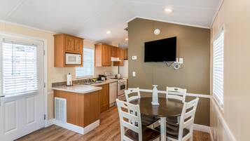 A compact kitchen with wooden cabinets, a microwave, a stove, and a dining table with chairs.
