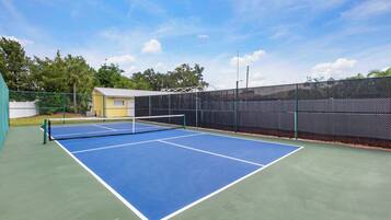 Una cancha de tenis al aire libre con red, rodeada por una valla y árboles.