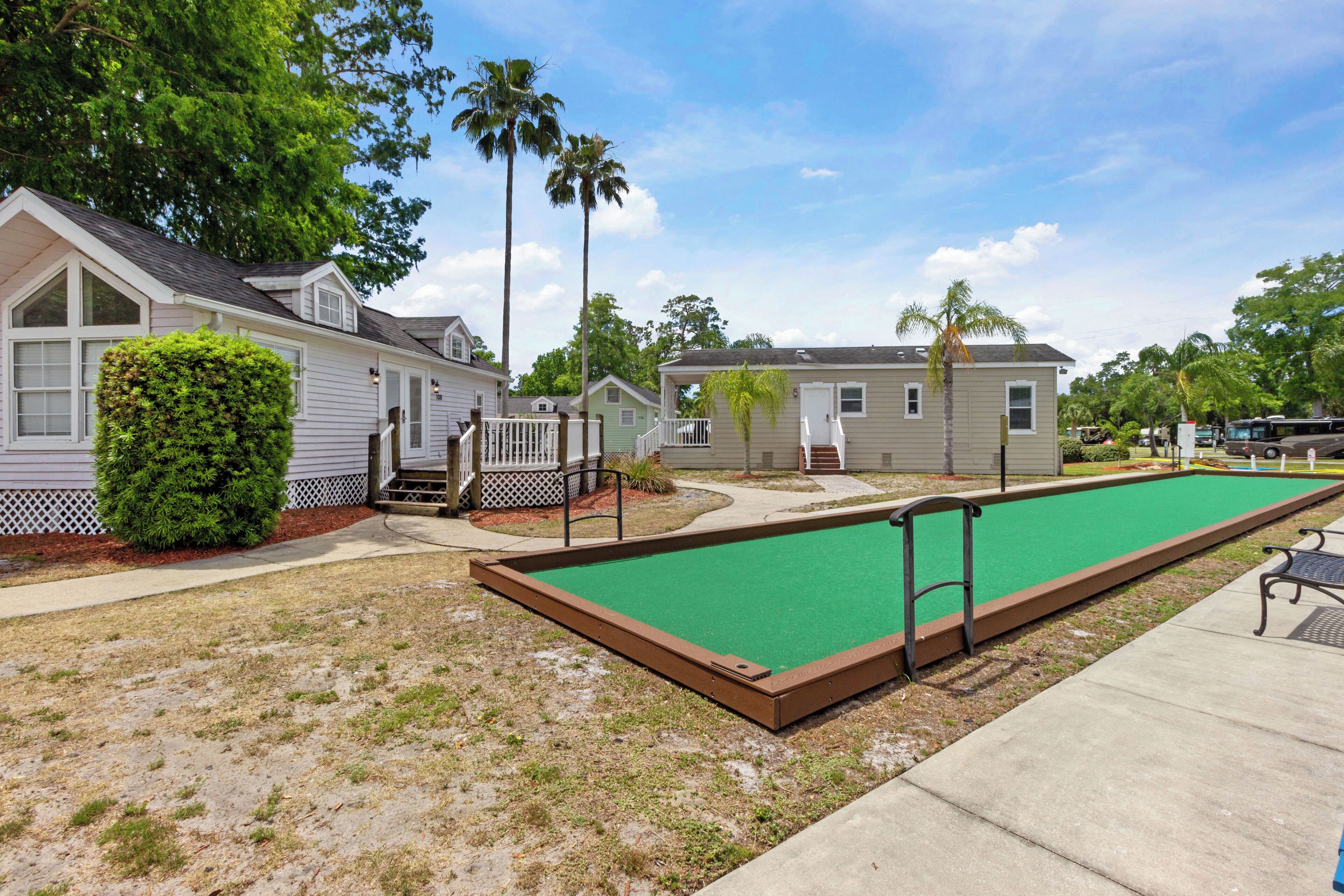 Un patio con un césped verde para croquet, una cerca blanca de piquetes y una hilera de viviendas móviles.