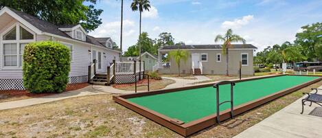 Un patio con un césped verde para croquet, una cerca blanca de piquetes y una hilera de viviendas móviles.