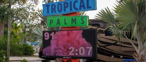 Un letrero con 'TROPICAL PALMS' y una pantalla digital que muestra la temperatura y la hora.