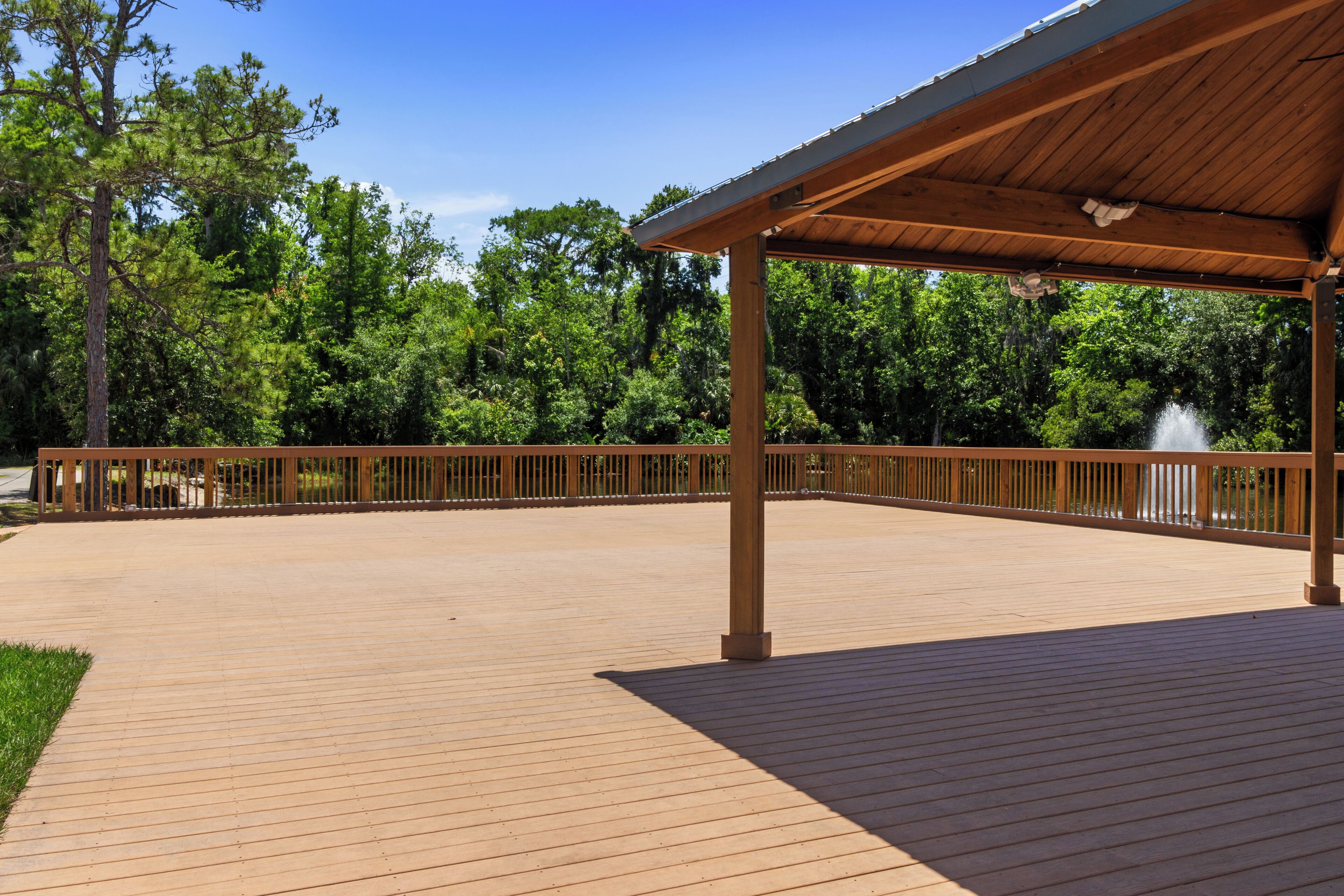 A covered wooden deck with a metal railing, surrounded by trees.