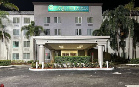A hotel entrance with a covered area, palm trees, and a sign for La Quinta Inn & Suites.