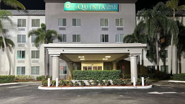 L’entrée d’un hôtel, avec un espace abrité, des palmiers et une enseigne indiquant « La Quinta Inn & Suites ».