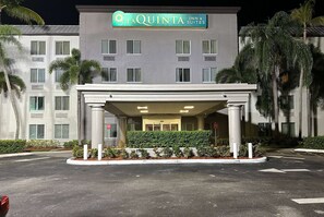A hotel entrance with a covered area, palm trees, and a sign for La Quinta Inn & Suites. - La Quinta Inn & Suites by Wyndham Sawgrass (Sunrise)