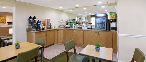 Comedor de hotel con armarios de madera, máquina de café, refrigerador y una pantalla de televisión.