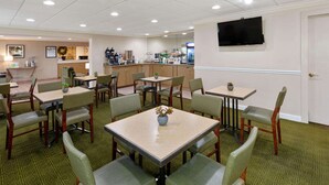 Un espace repas d’hôtel comprenant plusieurs tables et chaises, un coin café et un téléviseur fixé au mur.
