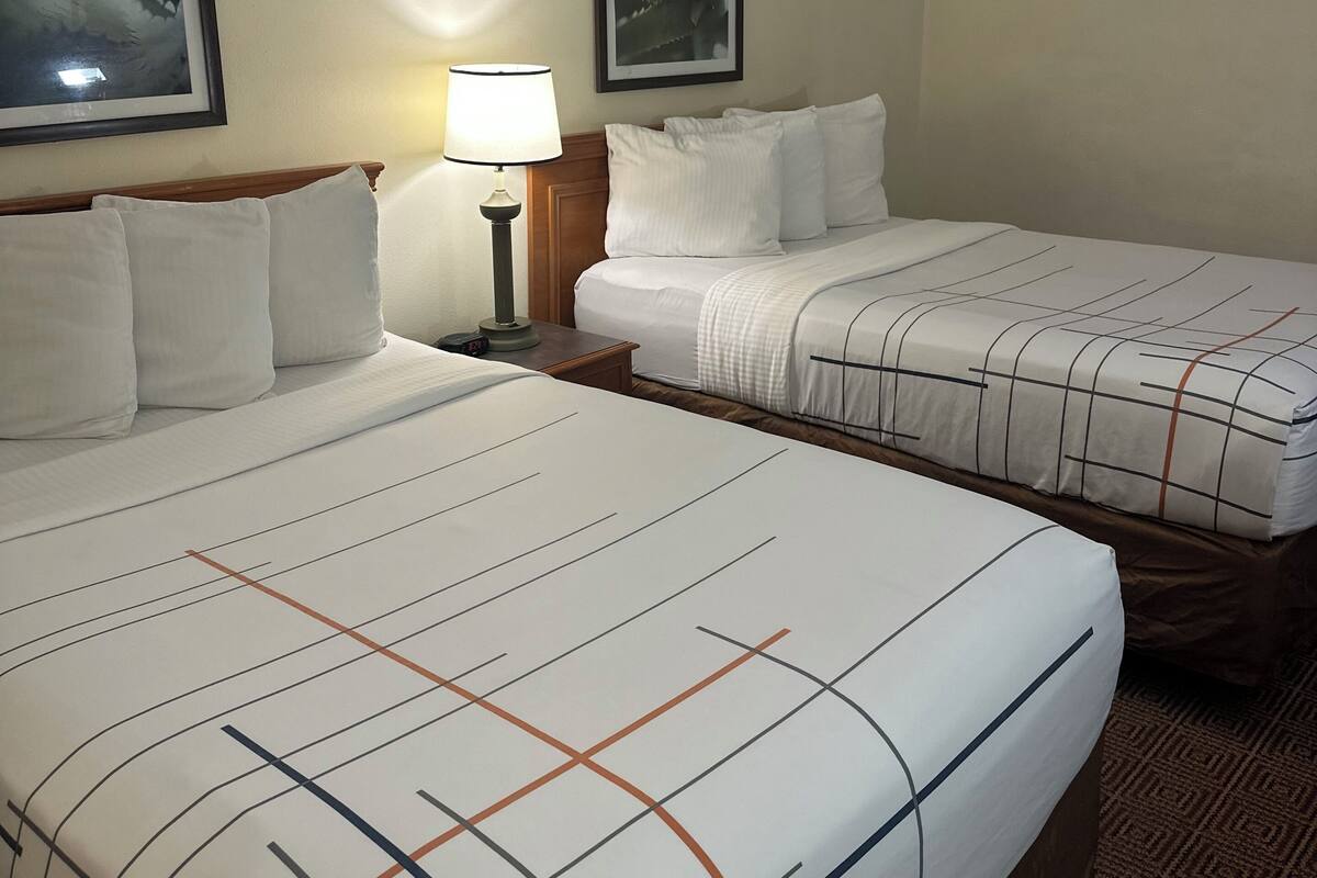 Ein Hotelzimmer mit zwei Betten, einem Nachttisch mit Lampe und zwei gerahmten Bildern an der Wand.