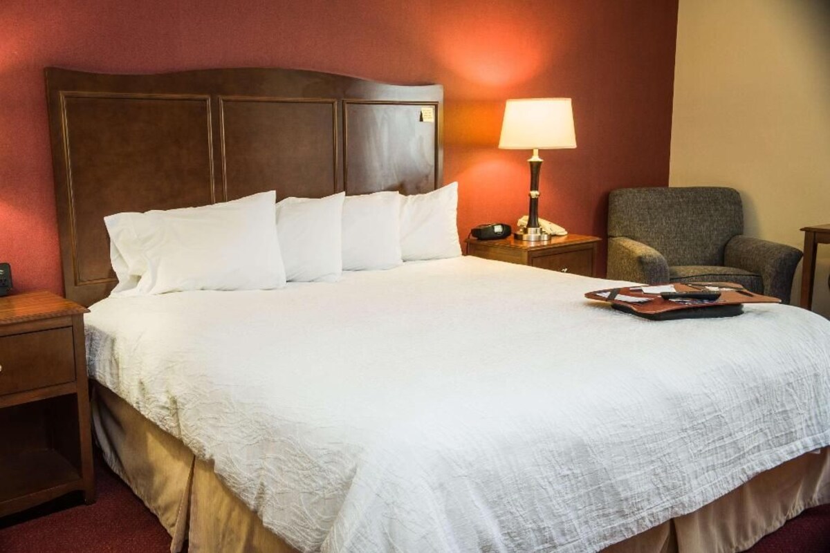 A hotel room with a large bed, a nightstand, a lamp, and a chair.