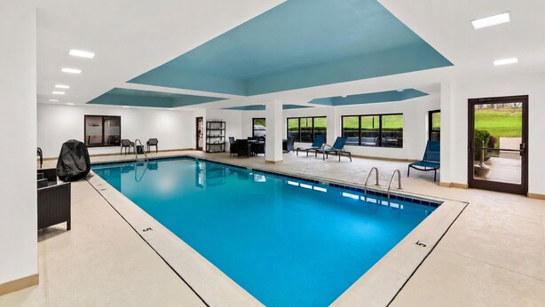 An indoor swimming pool with clear blue water, surrounded by lounge chairs and a sunbed, with a view of a grassy area through large windows. - Hampton Inn Lexington/Georgetown (Georgetown)