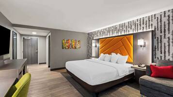 A modern hotel room with a large bed, a desk, a chair, and a sofa.