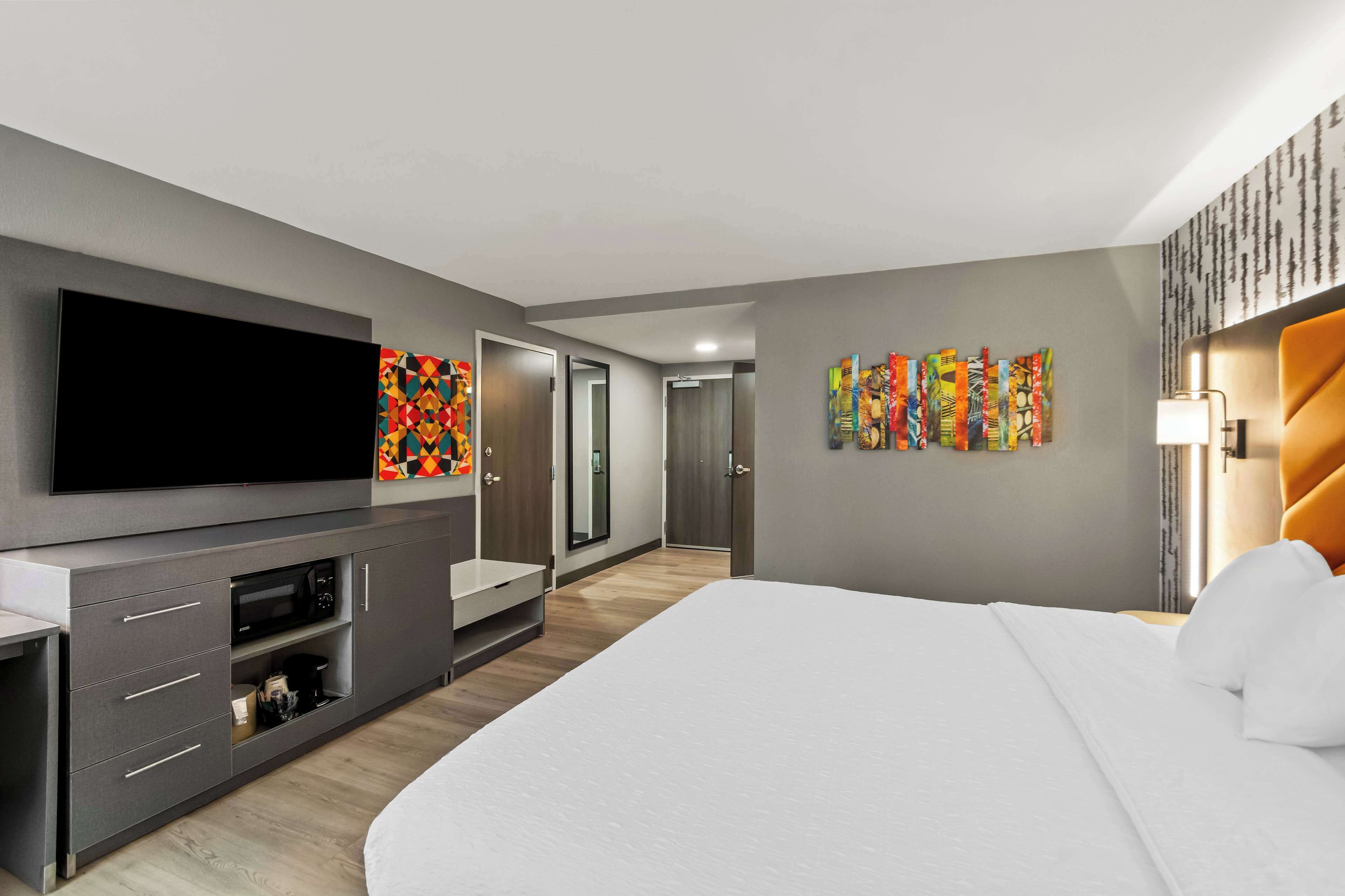 Ein modernes Hotelzimmer mit einem großen Bett, einem Flachbildfernseher, einer Mikrowelle und einer kleinen Sitzecke.