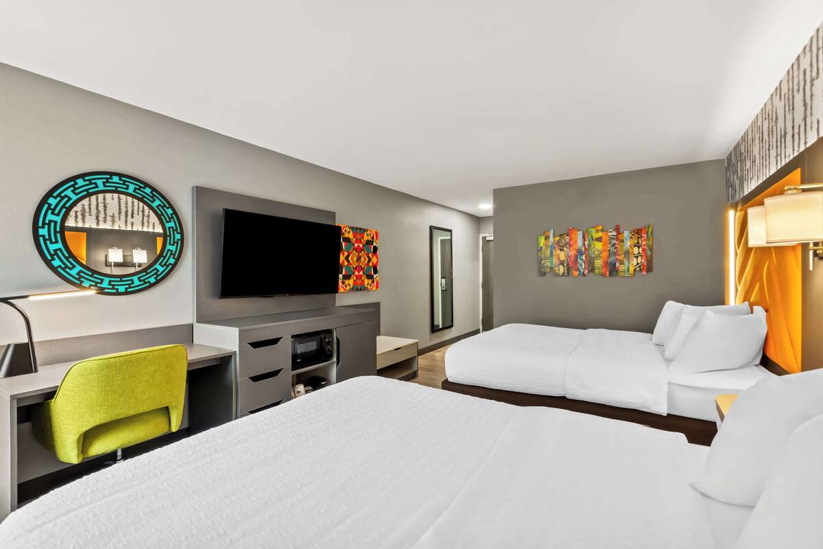 A hotel room with two beds, a desk with a chair, a flat-screen TV, a microwave, and a small table.