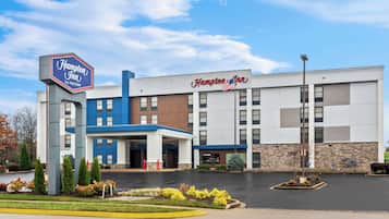 A Hampton Inn hotel with a modern design, featuring a prominent sign, a covered entrance, and a parking lot.