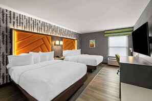 A hotel room with two beds, a desk, a TV, and a window.