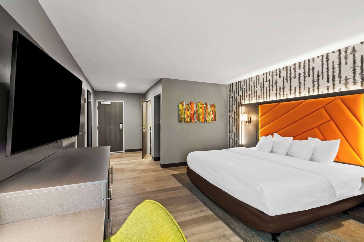 A modern hotel room with a large bed, a flat-screen TV, and a bright orange headboard.