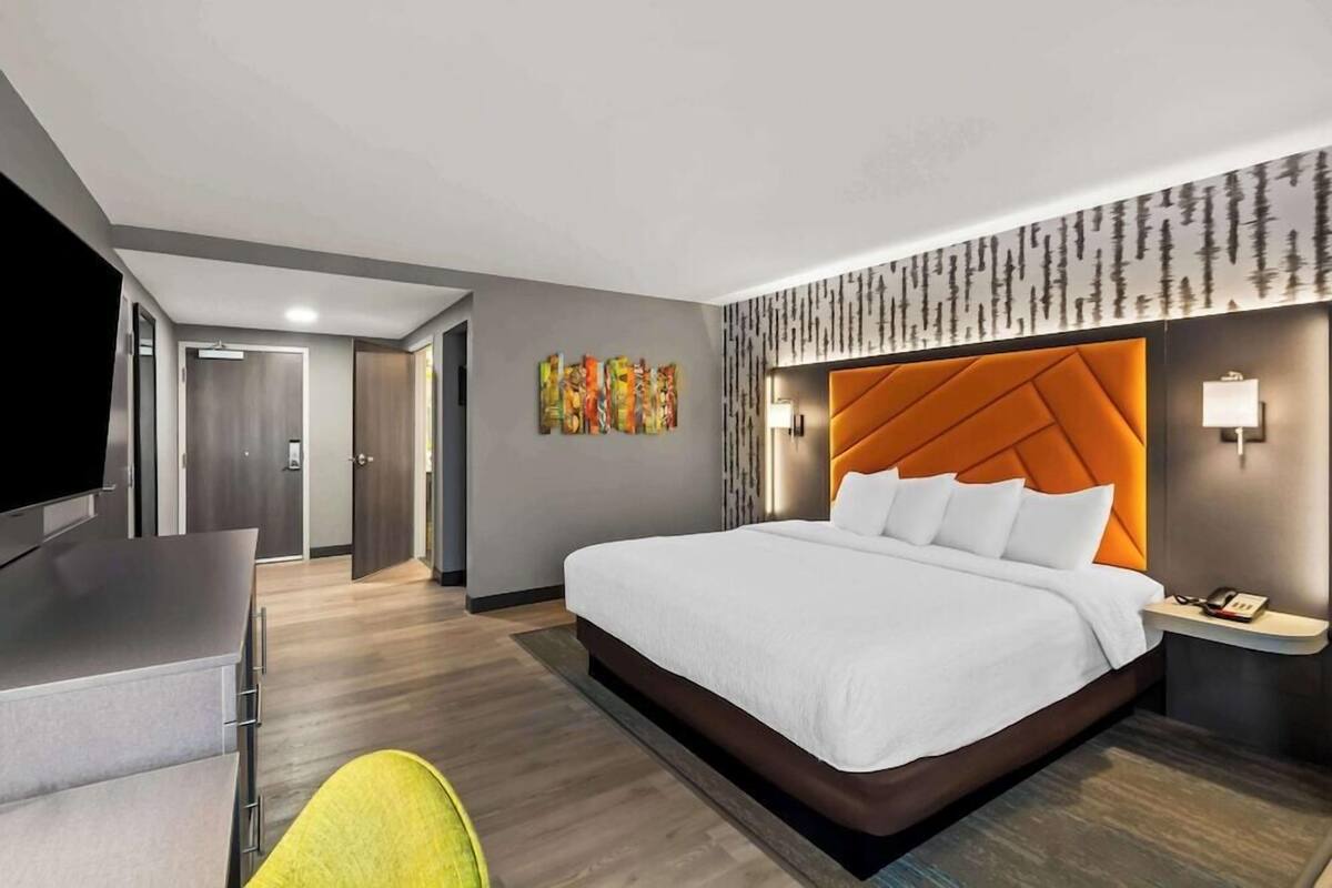 A modern hotel room with a large bed, a desk, a chair, and a television.